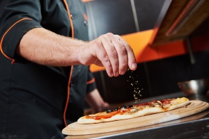 hand of chef baker in uniform adding spice into pizza after pizz