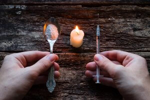 Male Addict Holding Syringe And Spoon With Heroin Next To A Cand